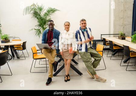 Gruppe positiver multirassischer Mitarbeiter, die auf Netbook surfen, während sie gemeinsam am Tisch im hellen modernen Büro an einem Geschäftsprojekt arbeiten Stockfoto
