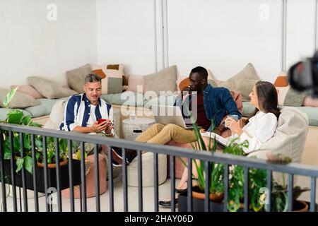 Ernste junge Frau mit langen welligen Haaren, die auf unscharfen Hintergrund die Kamera anschaut Stockfoto