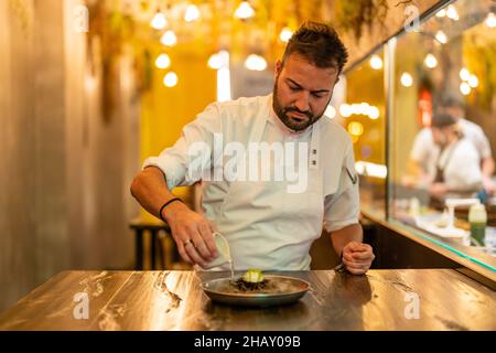 Mann gießt flüssigen Stickstoff aus Soße Boot auf Teller mit Seeigel in Molecular Cuisine Restaurant Stockfoto