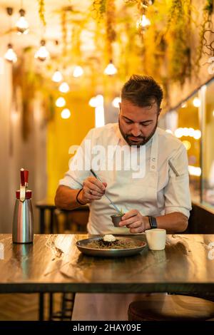 Bärtiger, professioneller Chefkoch, der Zutaten für Seeigel auf dem Teller am Tisch im modernen Restaurant zubereitet Stockfoto