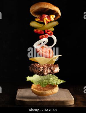 Fliegende Zutaten eines hochwertigen Fleischburgers, isoliert auf einem schlichten dunklen Hintergrund. Stockfoto