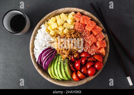 Draufsicht auf appetitlich bunte Poke Schüssel mit frischem Lachs und Reis serviert mit reifen Kirschtomaten Avocado Scheiben Zwiebel und Mango auf Beton gelegt Stockfoto