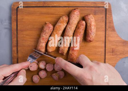 Von oben der Ernte anonymen Koch schneiden leckere gegrillte Würstchen auf Holz Schneidebrett auf dem Tisch Stockfoto