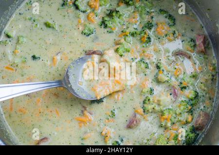 Von oben auf den Löffel in die Schüssel mit leckeren Sahnesuppe mit Brokkoli und Würstchen gelegt Stockfoto