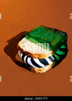 Sandwich in grüner schädlicher umweltfreundlicher Verpackung und mit Zebra-Füllung auf brauner Oberfläche in der Nähe der braunen Wand im hellen Studio platziert Stockfoto