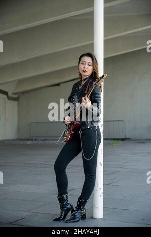 Porträt einer kantigen, gotischen asiatischen Frau, die Gitarre spielt Stockfoto