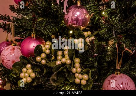 Weihnachtlicher Hintergrund von künstlichen Kiefernästen mit rosa und lila runden Kugeln mit Mustern und Zweigen mit weißem Geißblatt und grünen Blättern Stockfoto