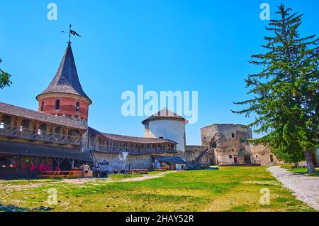 Der Hof des historischen Kamianets-Podilskyi Schlosses mit Holzgalerie auf dem Wall, konisch überdachten Türmen und der kleinen Taverne mit Open-Air-Kitc Stockfoto