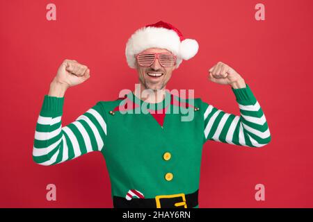 Glücklicher erfolgreicher Mann in Elf Kostüm und Partybrille. weihnachtsmann in weihnachtsmann Hut Stockfoto