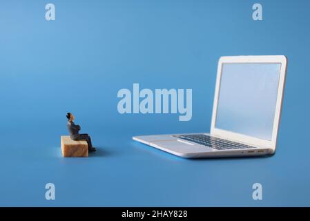 Online-Film-Streaming, Online-Meeting-Konzept. Miniatur-Mann sehen Film oder treffen auf Laptop. Blauer Hintergrund Stockfoto