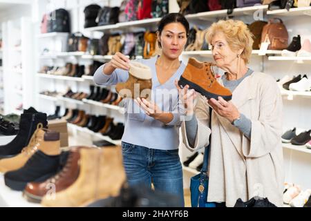 Verkäuferin hilft Oma bei der Auswahl neuer Schuhe Stockfoto