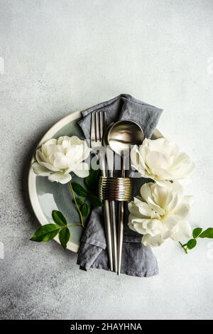 Set aus Besteck, Serviette, Serviettenring und weißen Rosen auf einem Teller Stockfoto