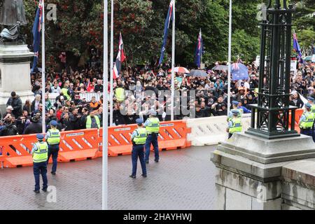 Wellington, Neuseeland. 16. Dezember 2021: Polizeibeamte, die den Eingang zum neuseeländischen Parlament bewachen, beobachten, wie junge Maori-Männer während eines Protests über Covid-19-Impfstoffbevollmächtigungen und Beschränkungen für nicht geimpfte Personen, die Bars, Restaurants und bestimmte andere Orte betreten, einen Haka durchführen. Die Impfraten sind niedriger und die Covid-Infektionen sind bei den Maori- und Pazifikinslandern höher als bei der Allgemeinbevölkerung. Quelle: Lynn Grieveson/Alamy Live News Stockfoto