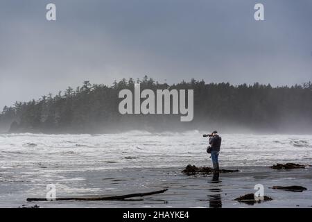 Mann, der an einem Strand steht und einen Sturm fotografiert, Tiofino, Vancouver Island, Vancouver, British Columbia, Kanada Stockfoto