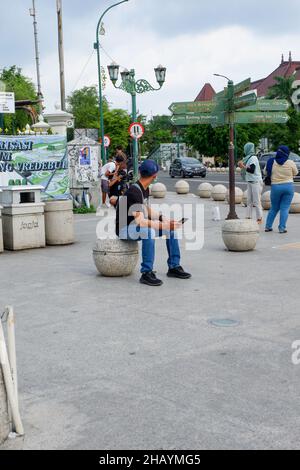 yogyakarta, Indonesien - November 20 2021 : Männer sitzen tagsüber auf Sitzplätzen im Stadtzentrum, während sie Handys spielen Stockfoto