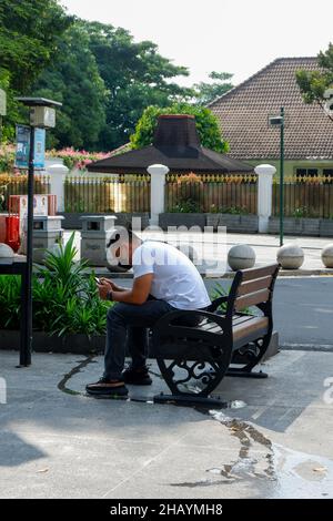 yogyakarta, Indonesien - November 20 2021 : Männer sitzen tagsüber auf Sitzplätzen im Stadtzentrum, während sie Handys spielen Stockfoto