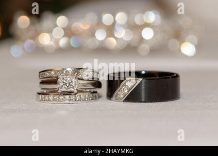 Weißgold und quadratische Diamanten Bräute Eheringe und Bräutigam schwarzen Ring mit Diamanten auf weißer Oberfläche mit Bokeh Stockfoto