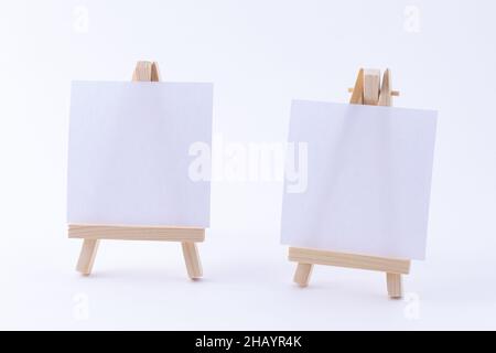 Zwei hölzerne Easels Miniature mit blanker weißer quadratischer Leinwand für Künstler und Maler - Mockup. Mini-Holzständer mit sauberer Zeichenfläche auf weißem Hintergrund, Copy Space Stockfoto