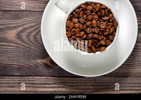 Auf einem alten Baum steht ein weißer Kaffeebecher gefüllt mit duftenden Kaffeebohnen Stockfoto