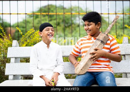 Glückliche indische multiethnische Kinder sprechen über Cricket mit Fledermaus und Ball sitzen im Park - Konzept der Kindheit Freundschaft, Urlaub, Urlaub Stockfoto