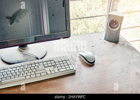 Alte Tastatur mit Maus und kaputter Monitor mit Audio-Lautsprecher sind auf einem Holztisch und in einer Werkstatt mit dickem Staub bedeckt Stockfoto