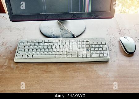 Alte Tastatur mit Maus und kaputtem Monitor stehen auf einem Holztisch und sind in einer Werkstatt mit dickem Staub bedeckt. Draufsicht Stockfoto