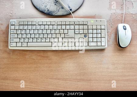 Alte Tastatur mit Maus und kaputtem Monitor stehen auf einem Holztisch und sind in einer Werkstatt mit dickem Staub bedeckt. Draufsicht Stockfoto