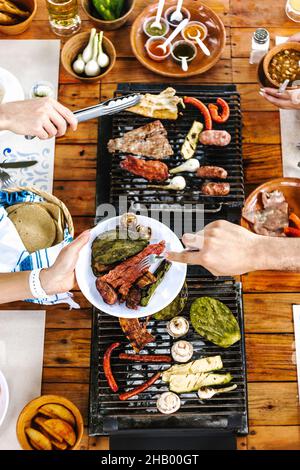 Eine Gruppe lateinischer Freunde, die mexikanische Tacos und traditionelles Essen, Snacks und die Hände der Menschen über den Tisch essen, Draufsicht. Mexikanische Küche Lateinamerika Stockfoto