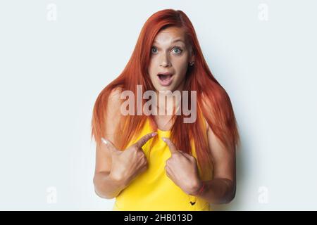 Schockierte rothaarige Frau zeigt auf sich selbst mit Zeigefinger, überrascht beschuldigt werden. Modisches Porträt. Studioaufnahme. Stockfoto