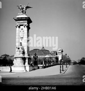 Paris Pont Alexandre III mit dem Ruf der Industrie (Renommée de l'Industrie) Bronzeskulptur, 1945. Die Kamera zeigt vom linken Ufer der seine auf die berühmt-reich verzierte Flussbrücke, wobei einer der vier Maurersockeln das Bild auf der linken Seite dominiert. Das geschnitzte Mauerwerk ist von Louis XIV. Es gibt keine Menschen auf dem Gehweg und keine Fahrzeuge auf der Brückenstraße. Der Grand Palais ist im Hintergrund des Bildes zu sehen. Nur sechs Monate vor diesem Foto diente dieser Palast als Hauptquartier der deutschen SS in Paris. Stockfoto