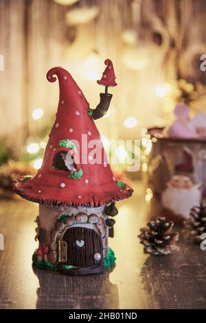 Handgemachtes Lehmhaus mit einem Dach in Form einer Fliegenagarie auf dem Hintergrund einer glühenden Girlande und Weihnachtsdekor. Stockfoto