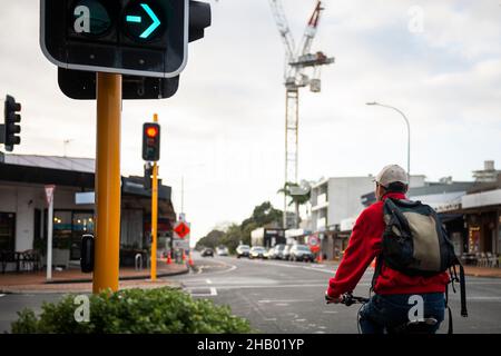 Ein Radfahrer, der auf der Stadtstraße fährt und an der Kreuzung mit oranger Ampel hält. Unscharf Reduzieren Sie Geschwindigkeit Straßenschild und Bau cra Stockfoto