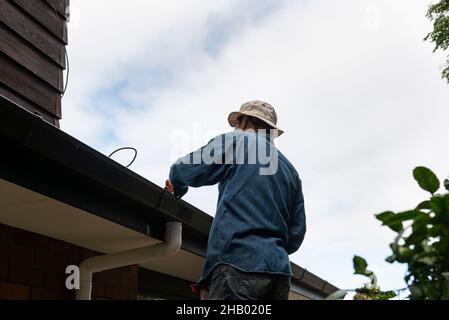 Mann, der auf einer Leiter stand, das Dach reinigte und reparierte. Hauswartung. Stockfoto