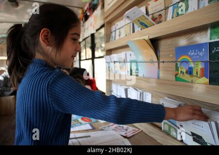 Kabul, Afghanistan. 14th Dez 2021. Ein Kind sucht am 14. Dezember 2021 in einer mobilen Bibliothek in Kabul, der Hauptstadt Afghanistans, nach einem Cartoon-Buch. Inspiriert von einer Gruppe afghanischer Jugendlicher bietet eine lokale Wohltätigkeitsgruppe kostenlose mobile Bibliotheksdienste für Kinder in dem vom Krieg zerrissenen Kabul an.ZUM ARTIKEL "Feature: Afghan public Library strebt danach, "Buch für alle" inmitten eines langen Krieges bereitzustellen.Quelle: Saifurahman Safi/Xinhua/Alamy Live News Stockfoto