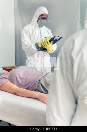 Ärzte in bakteriologischem Schutz, die einen Patienten auf einer Liege medizinisch untersuchen Stockfoto