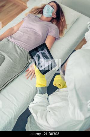 Arzt im Schutzanzug, der die Röntgenaufnahme des Patienten auf einer Tablette untersucht Stockfoto