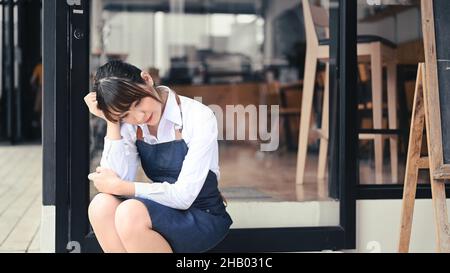 Gestresste Unternehmerin aus Kleinunternehmen, die vor ihrem Café sitzt. Stockfoto