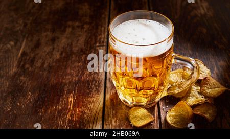 Oben vom Bier in der Glastasse, die auf dem hölzernen Tisch mit den salzigen Kartoffelchips aufgestellt ist Stockfoto