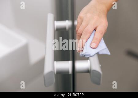 Reinigen Sie die Griffe der Glastür mit einem antiseptischen, feuchten Tuch. Frau Hand mit Handtuch für die Reinigung Zimmer Tür Link. Desinfizieren von Oberflächen in Stockfoto