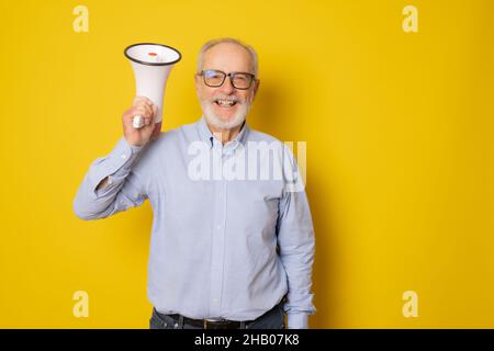 Senior lächelnder Mann mit Megaphon isoliert auf gelbem Hintergrund. Stockfoto