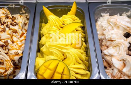 Mango-Eis mit Fruchtstücken von oben. Verschiedene Eiscreme in Tabletts in der Eisdiele. Stockfoto