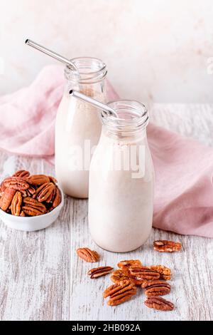 Alternative nicht-Milchprodukte hausgemachte Pekannüsse in Glasflaschen mit wiederverwendbaren Trinkhalmen aus Metall. Pekannussmilch auf Holzplatte Stockfoto