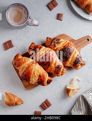 Frisch gebackene Schokoladencroissants und Becher mit Cappuccino auf grauem Betontisch. Französisches Frühstück, flach liegend, Blick von oben Stockfoto