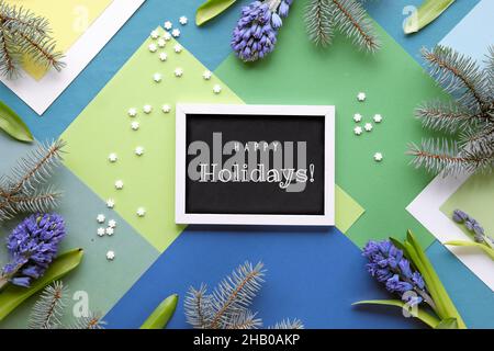 Text Frohe Feiertage auf Tafel. Grün geschichteten geometrischen Papier Hintergrund mit blauen Hyazinthen Blumen und Tannenzweigen. Winterliche Dekoration Stockfoto