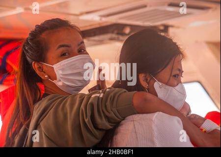 2 Frauen, inländische Touristen, (1 Kambodschaner, links, 1 gemischte Rassen, Rechts, 1/4 Vietnamesen, 1/4 Cham, 1/4 Chinesen und 1/4 Kambodschaner), mit schützenden Gesichtsmasken, fahren Sie mit der Fähre nach Saracen Bay, Koh Rong Samloem während der COVID - Pandemie 19. Golf von Thailand, Provinz Sihanoukville, Kambodscha. 6th. Dezember 2021. © Kraig Lieb Stockfoto