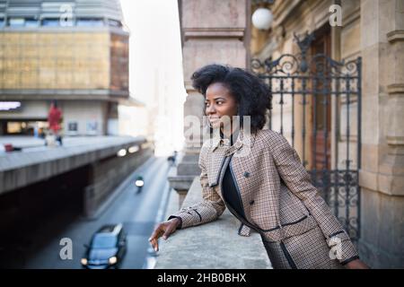 Schöne afroamerikanische junge Frau mit Afro und großen Reifringen in einem stilvollen Mantel. Stadtleben Konzept, Street Portrait. Frühlings- oder Herbstzeit. Selektiver Fokus, Kopierbereich Stockfoto