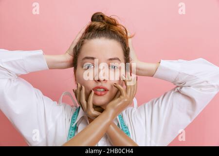 Nahaufnahme eines lächelnden Mädchens, Schneiderin, die die Hände der Schaufensterpuppe isoliert auf rosa Hintergrund hält. Konzept des Jobs, Hobby Stockfoto