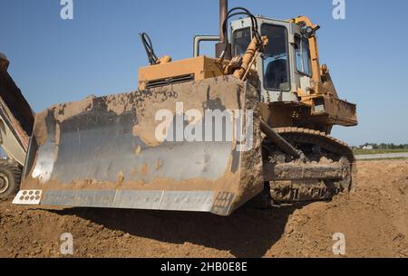 An einem heißen, sonnigen Tag arbeitet auf einer Baustelle ein kraftvoller, schwerer Raupenraupe. Baumaschinen für Erdarbeiten. Planierschilde aus nächster Nähe Stockfoto