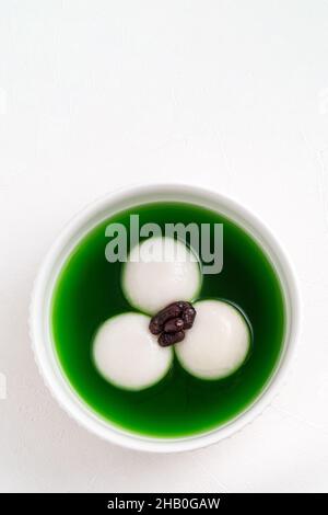 Draufsicht auf Matcha Big tangyuan (tang Yuan) mit süßer Matcha-Suppe und roter Bohnenpaste in einer Schüssel auf weißem Tischhintergrund für Festessen. Stockfoto