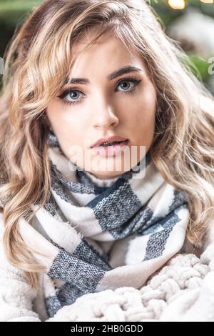 Porträt einer lockigen blonden Frau mit Strickpullover und kariertem Schal vor einem weihnachtsbaum. Stockfoto